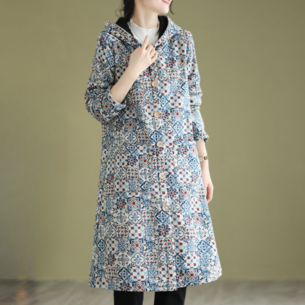 Vrouw draagt lange, kleurrijke jas met geometrisch patroon en knopen, tegen een neutrale achtergrond. Modieuze dameskleding, herfst/winter stijl.