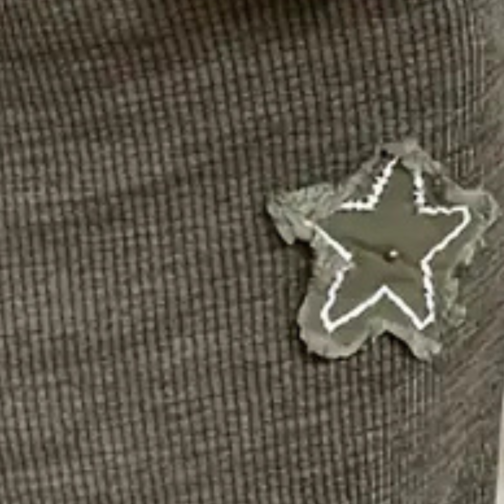 Grijze geribbelde stof met een groene stervormige patch, versierd met witte stiksels. Ideaal voor modeaccessoires en textielontwerp.