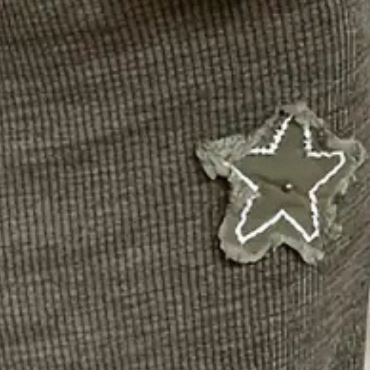 Grijze geribbelde stof met een groene stervormige patch, versierd met witte stiksels. Ideaal voor modeaccessoires en textielontwerp.