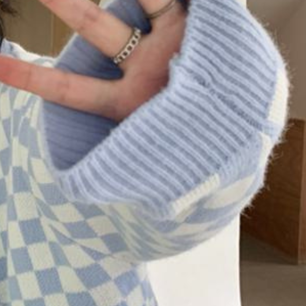 Blauwe en witte geruite trui met ribgebreide mouw, hand met zilveren ringen. Modieuze dameskleding, wintertrui, trendy accessoires.
