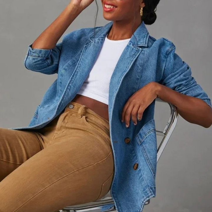 Vrouw in casual stijlvolle denim jas, witte top en bruine broek, zittend op een stoel. Trendy damesmode, denim jas, casual outfit.