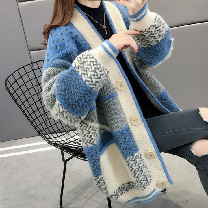Vrouw draagt een gebreid oversized vest met blauwe en grijze patronen, zittend op een moderne draadstoel. Wintermode, comfortabele dameskleding.