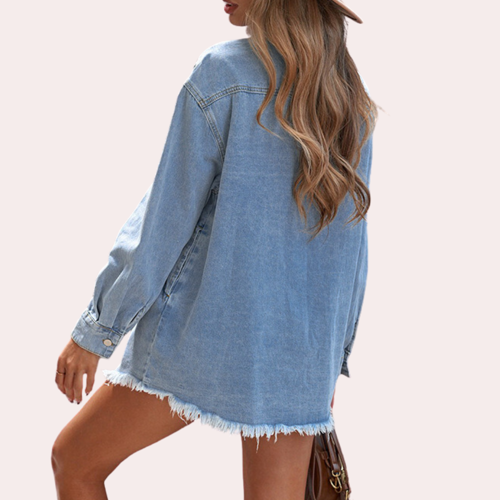 Vrouw in oversized denim jas met rafelige zoom, draagt een hoed en houdt een bruine tas vast. Modieuze casual outfit, trendy dameskleding.