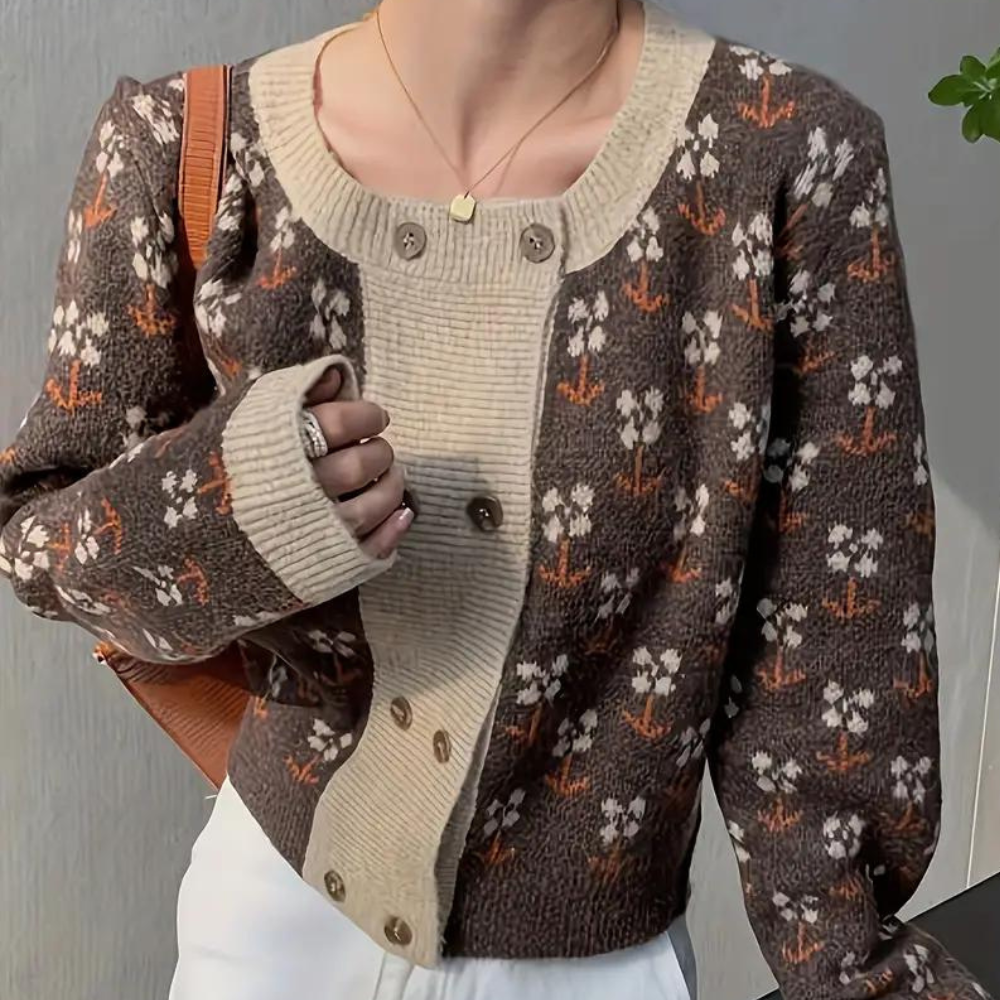 Bruin gebreid vest met bloemenpatroon, crèmekleurige knopenlijst, gedragen door persoon met witte broek en bruine tas. Modieuze herfstkleding.