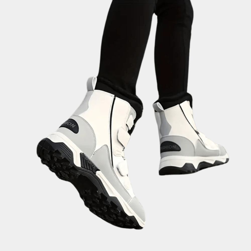 Witte winterlaarzen met zwarte zool, gedragen door persoon in zwarte broek. Modieuze, waterdichte schoenen voor koude weersomstandigheden.