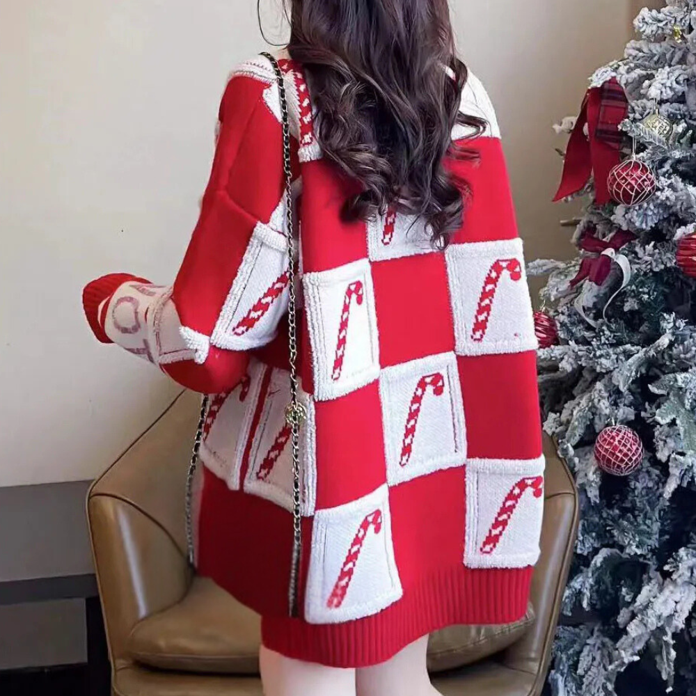 Vrouw in rode kersttrui met zuurstokpatroon, zittend naast versierde kerstboom. Perfect voor feestelijke wintermode en kerstcadeau-ideeën.