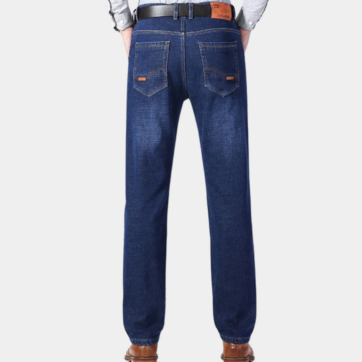 Donkerblauwe spijkerbroek voor heren, achteraanzicht. Klassiek ontwerp met rechte pijpen, leren riem en bruine schoenen. Perfect voor casual outfits.