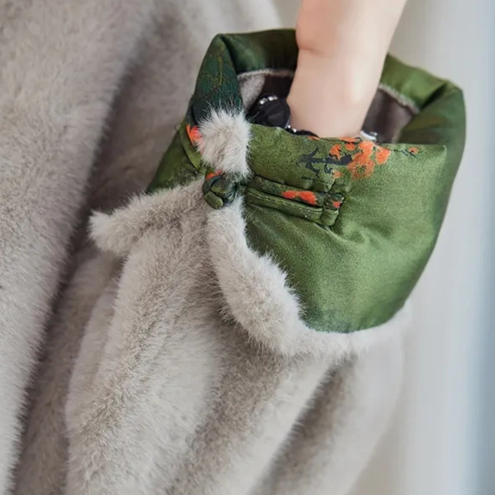 Grijze bontjas met groene satijnen voering en bloemenprint, close-up van mouw met hand erin. Luxe wintermode, warme dameskleding.