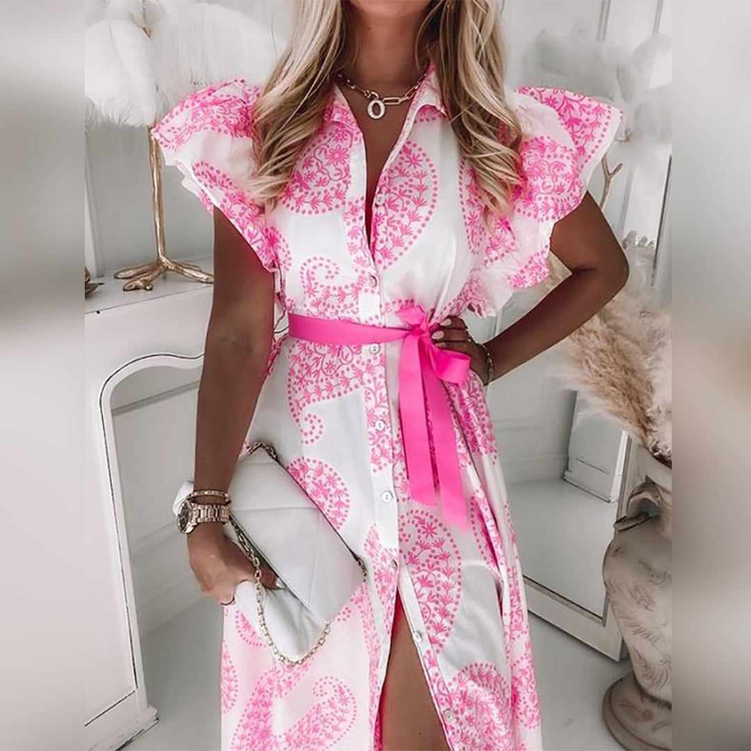 Vrouw in roze-witte paisley jurk met strikceintuur, staand voor spiegel. Zomermode, elegante dameskleding, trendy outfit.