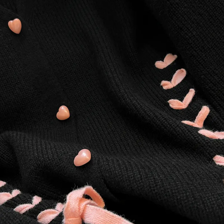 Zwarte gebreide stof met roze hartvormige knopen en lintdetails, modieuze textielaccessoires, close-up van trendy kledingontwerp.