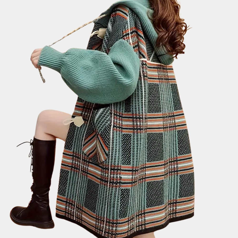 Vrouw in geruite jas met groene capuchon en gebreide mouwen, zittend met zwarte laarzen. Modieuze winterkleding, trendy damesmode.