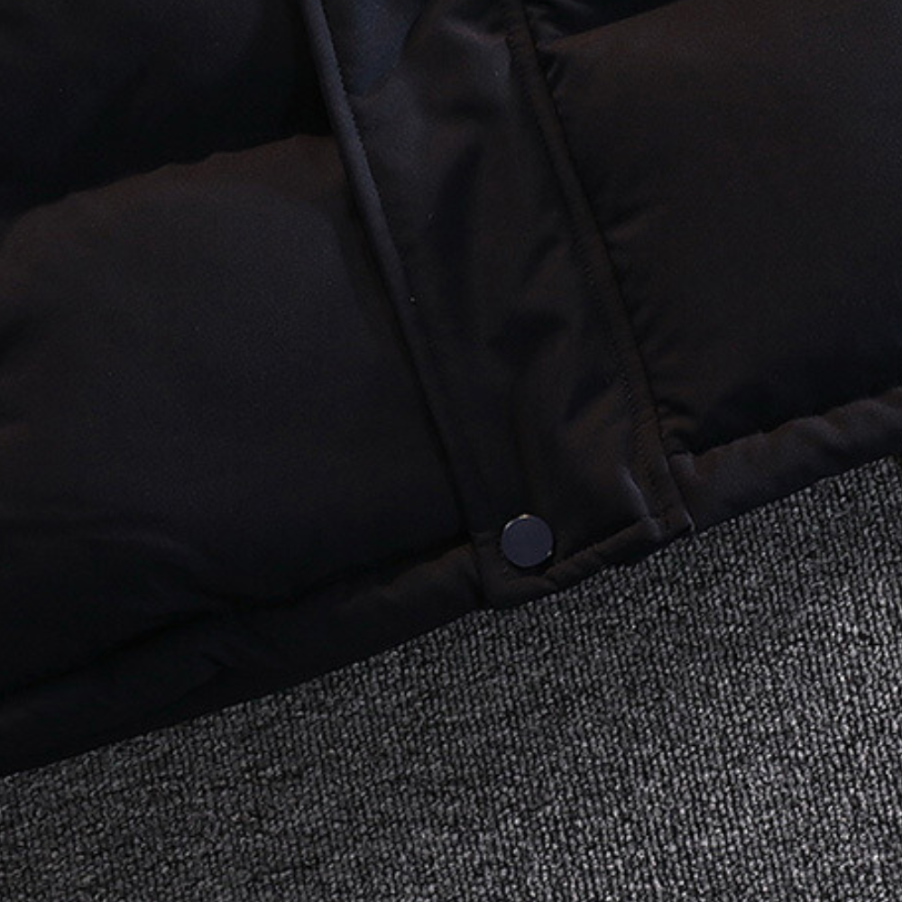 Zwarte gewatteerde winterjas op grijze stoffen achtergrond, close-up van knoop en stiksel. Perfect voor koude weersomstandigheden.