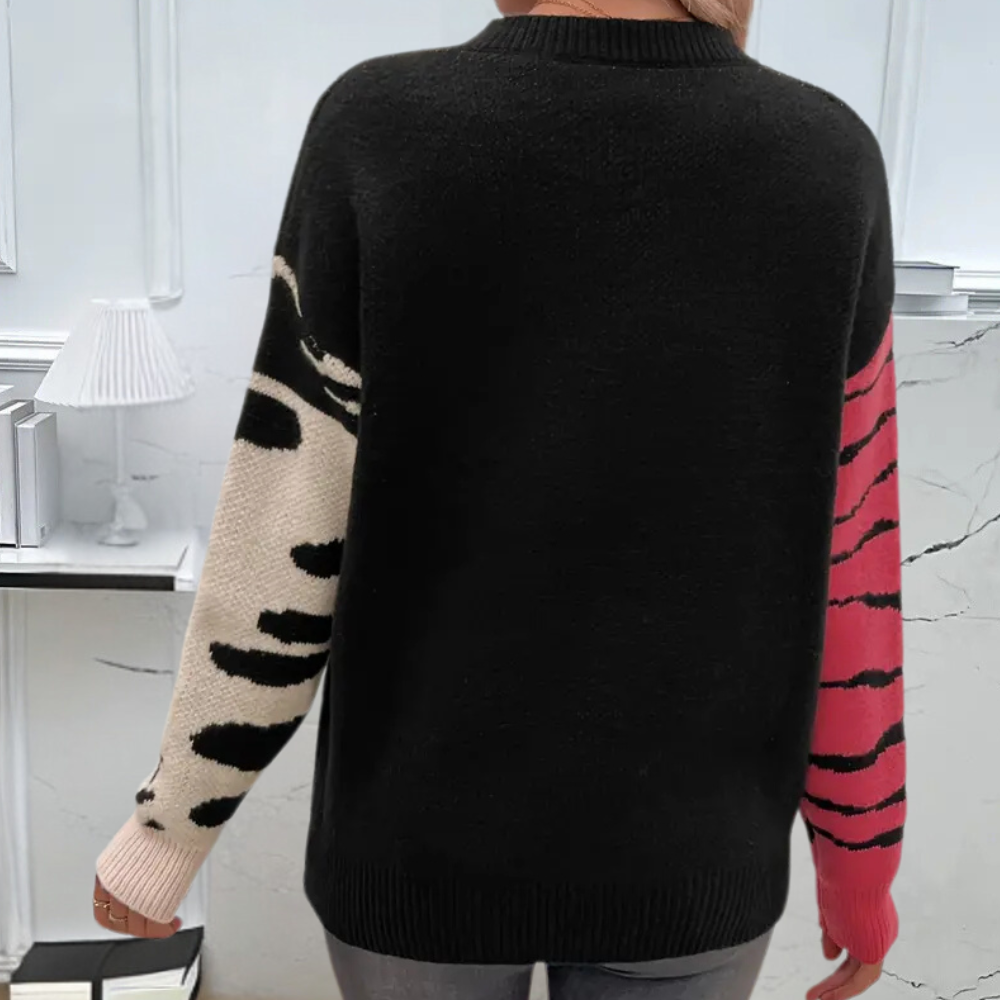 Zwarte trui met contrasterende mouwen; linker mouw beige met zwarte vlekken, rechter mouw roze met zwarte strepen. Trendy damesmode, herfstkleding.