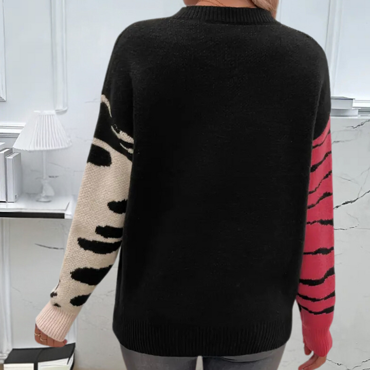 Zwarte trui met contrasterende mouwen; linker mouw beige met zwarte vlekken, rechter mouw roze met zwarte strepen. Trendy damesmode, herfstkleding.