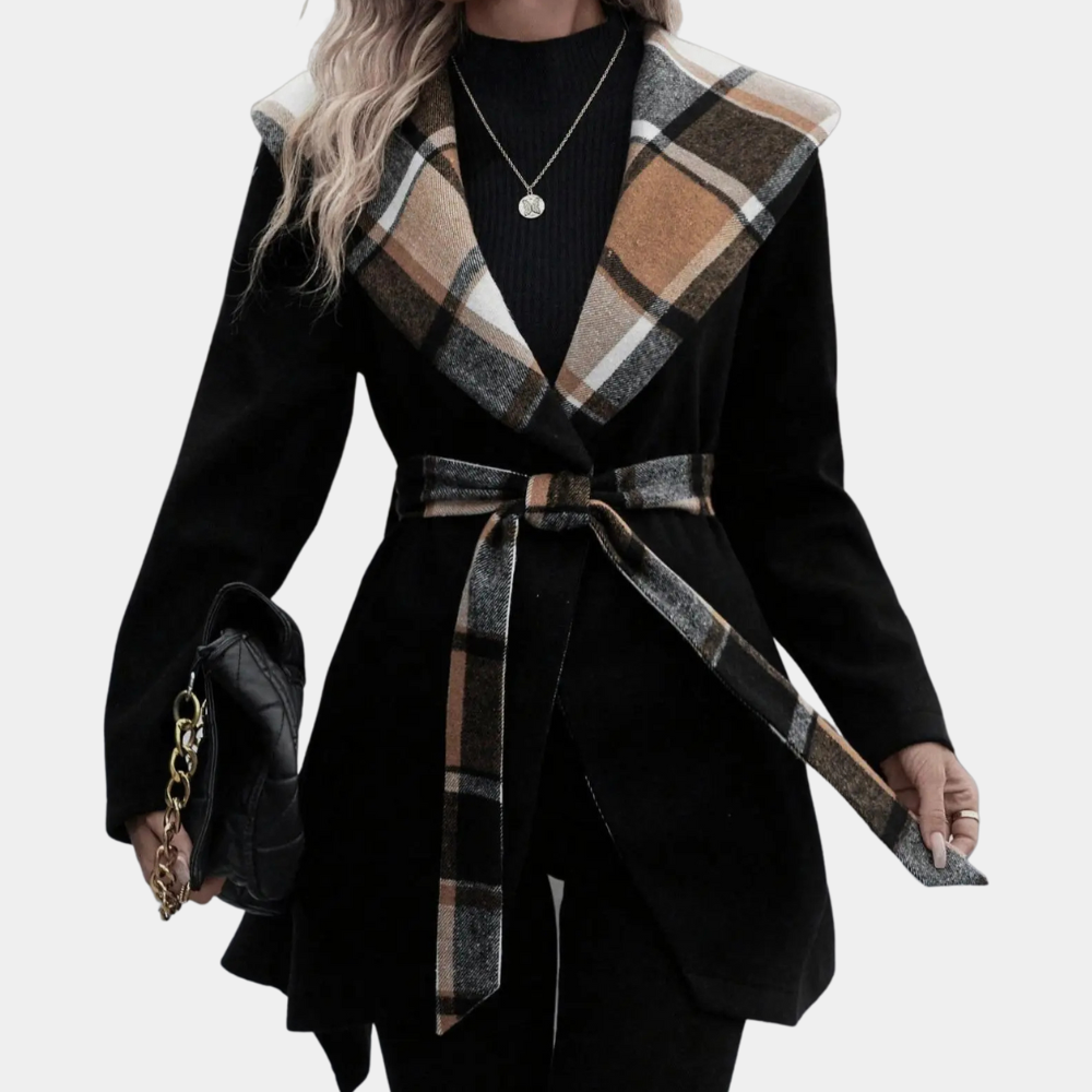 Vrouw in zwarte jas met geruite kraag en ceintuur, draagt een zwarte tas met gouden ketting. Modieuze dameskleding, herfst/winter stijl.
