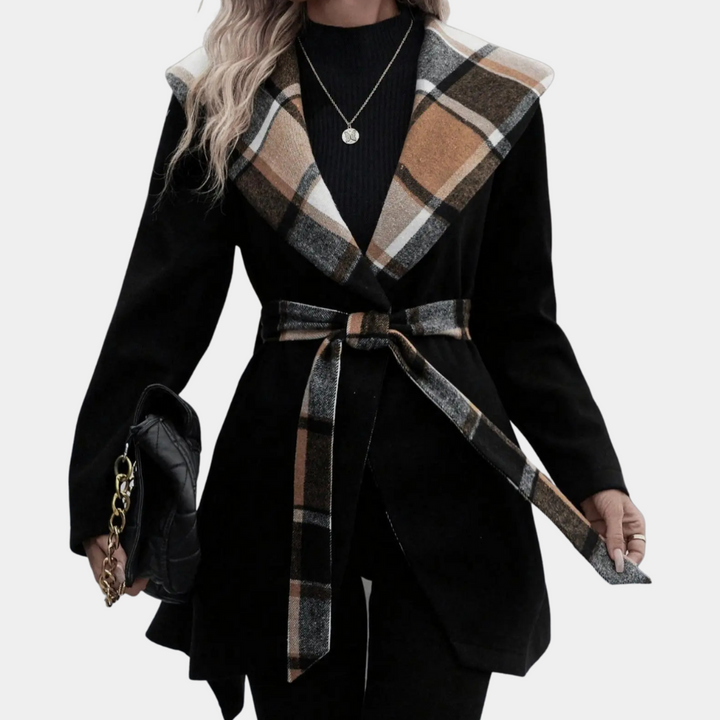 Vrouw in zwarte jas met geruite kraag en ceintuur, draagt een zwarte tas met gouden ketting. Modieuze dameskleding, herfst/winter stijl.