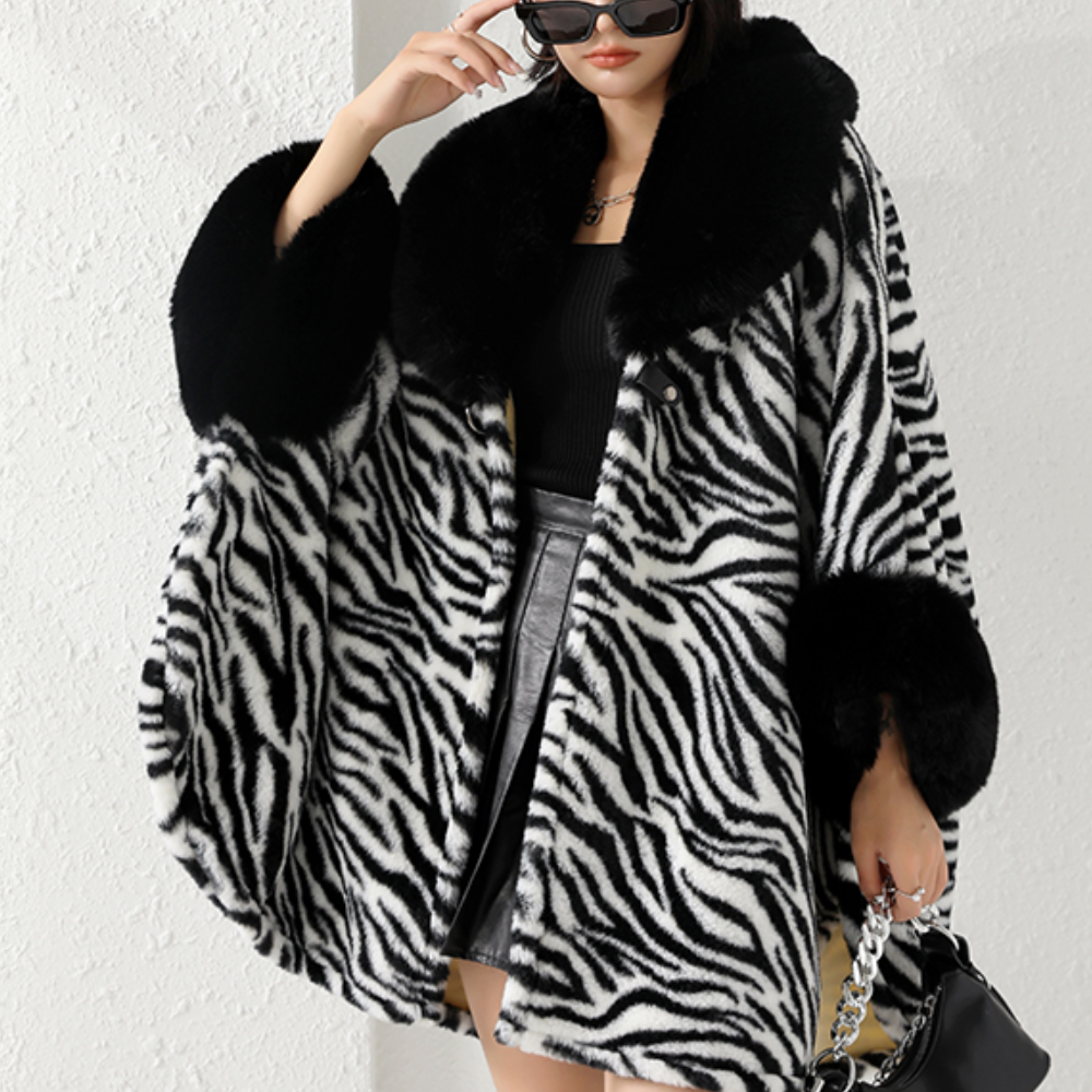 Vrouw in zebraprint jas met zwarte kraag en manchetten, draagt zonnebril en zwarte rok, houdt een handtas vast. Modieuze winterkleding.