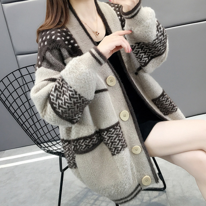 Vrouw draagt een oversized gebreid vest met bruine en beige patronen, zittend op een moderne zwarte draadstoel. Wintermode, comfortabele kleding.