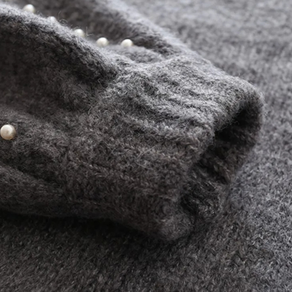 Donkergrijze gebreide trui met pareldecoratie, close-up van mouw. Zachte wol, stijlvolle damesmode, herfst- en winterkleding.