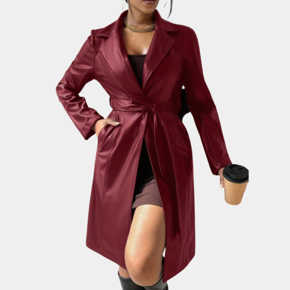 Vrouw in bordeauxrode leren trenchcoat met ceintuur, zwarte jurk en laarzen, houdt een koffiebeker vast. Stijlvolle herfstmode, trendy dameskleding.