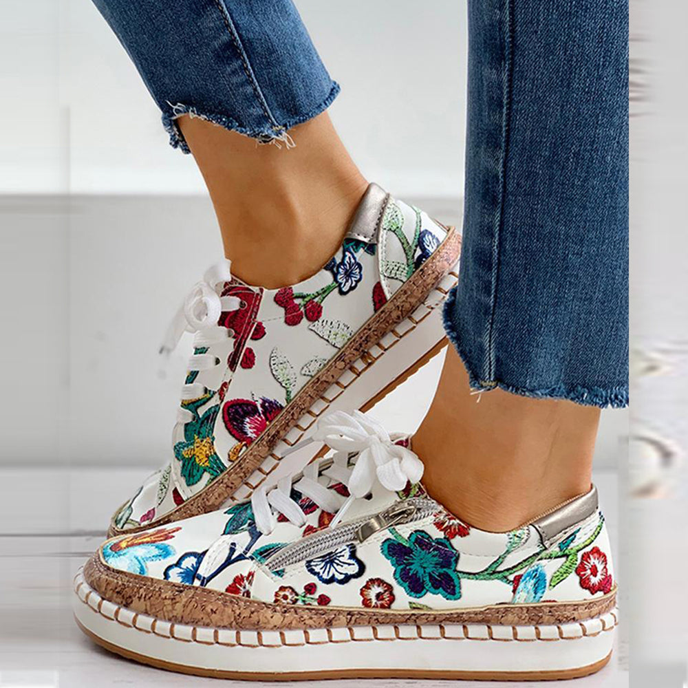 Witte sneakers met kleurrijke bloemenprint, gevlochten zool en witte veters, gedragen met blauwe jeans. Trendy damesmode, casual schoenen.