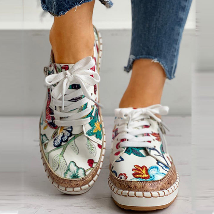Witte sneakers met kleurrijke bloemenprint, gevlochten zool en witte veters, gedragen met blauwe jeans. Trendy damesmode, casual schoenen.