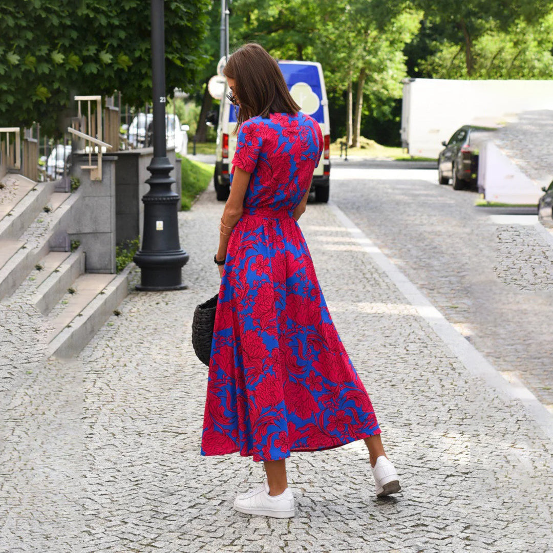 Vrouw in rood-blauwe bloemenjurk op straat, zomermode, casual stijl, sneakers, stedelijke achtergrond, trendy dameskleding, buiten wandelen.