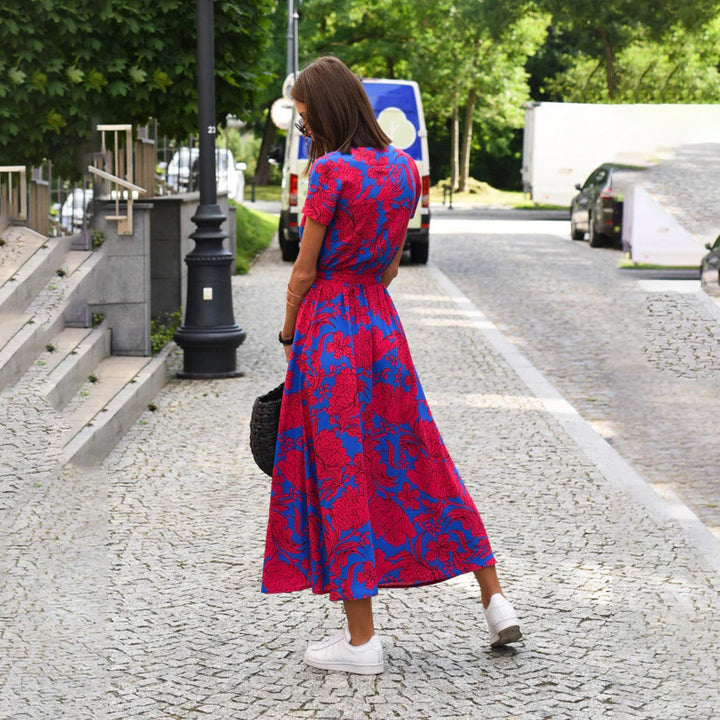 Vrouw in rood-blauwe bloemenjurk op straat, zomermode, casual stijl, sneakers, stedelijke achtergrond, trendy dameskleding, buiten wandelen.