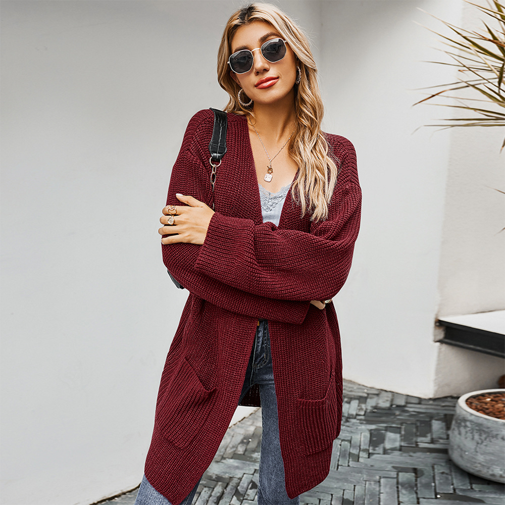 Vrouw in bordeauxrode gebreide cardigan, zonnebril en jeans, poseert buiten. Modieuze herfstkleding, casual damesstijl, trendy outfit.