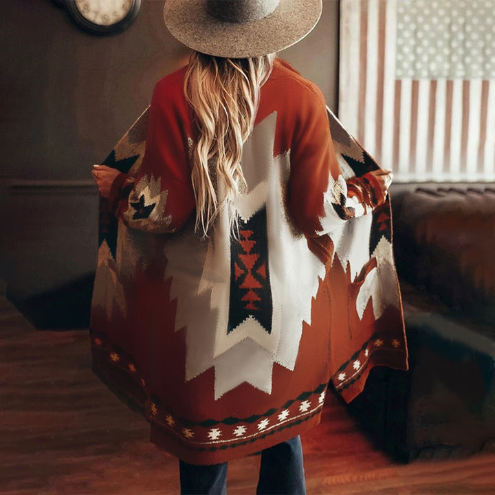 Vrouw in rode, geometrisch patroon poncho en hoed, binnen in woonkamer. Boho-chic mode, herfstkleding, trendy dameskleding.