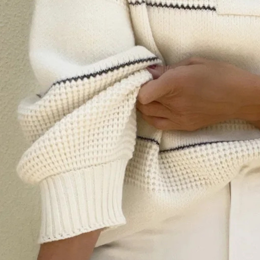 Witte gebreide trui met geribbelde mouwen en zwarte stiksels, gedragen door persoon. Modieuze dameskleding, herfst-winter stijl.