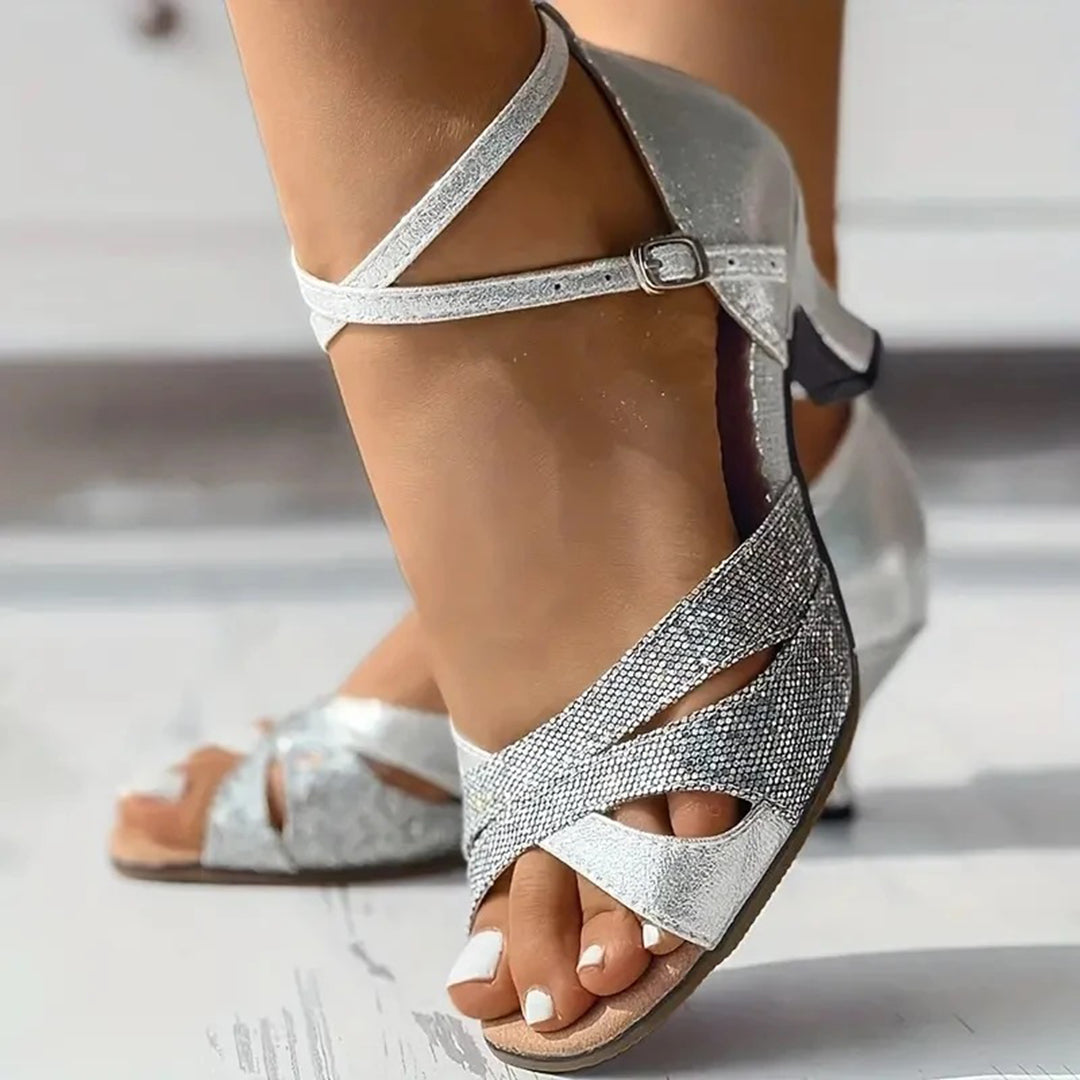 Zilveren dansschoenen voor dames met open teen en kruisbandjes, ideaal voor salsa of ballroom. Elegante hak en glinsterende afwerking.