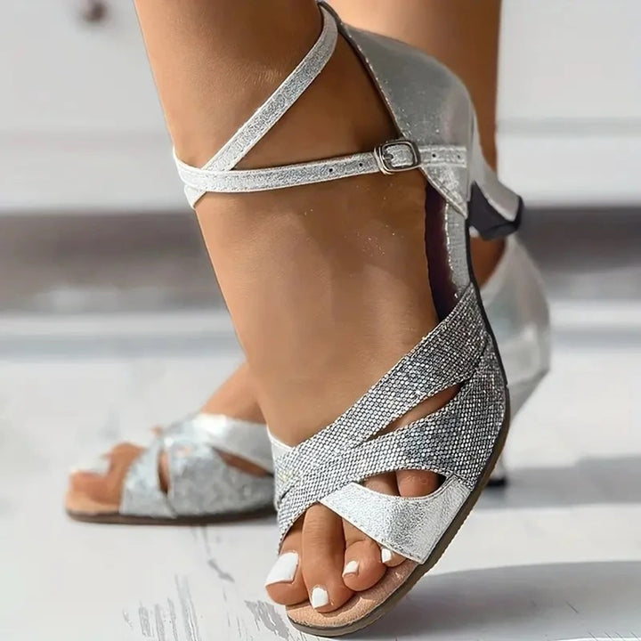 Zilveren dansschoenen voor dames met open teen en kruisbandjes, ideaal voor salsa of ballroom. Elegante hak en glinsterende afwerking.