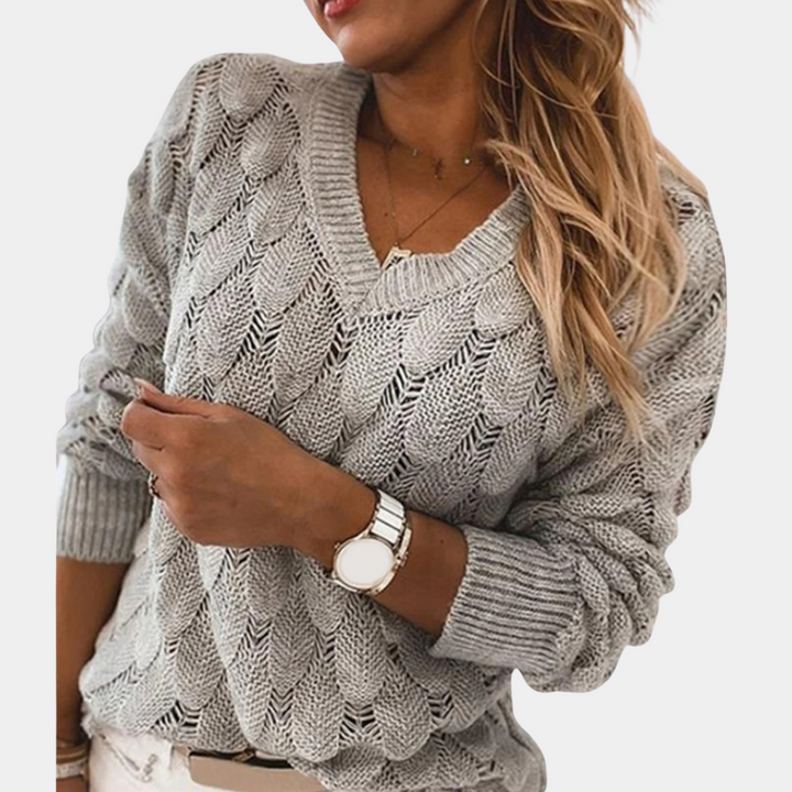Grijze gebreide damestrui met V-hals, gedragen door model. Modieuze, comfortabele trui voor herfst en winter. Perfect voor casual outfits.