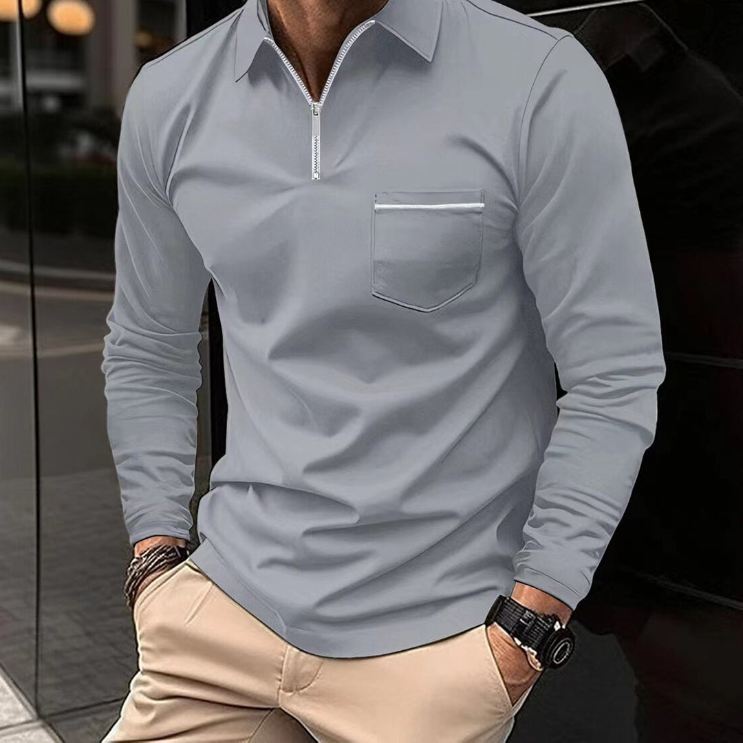Grijze herenpolo met lange mouwen en ritssluiting, borstzak, gedragen door model. Stijlvolle casual herenkleding, ideaal voor dagelijks gebruik.