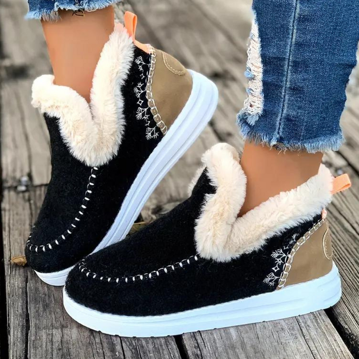 Zwarte winterlaarzen met witte zool en beige voering, gedragen met gescheurde jeans op houten vloer. Warme dames schoenen, trendy en comfortabel.