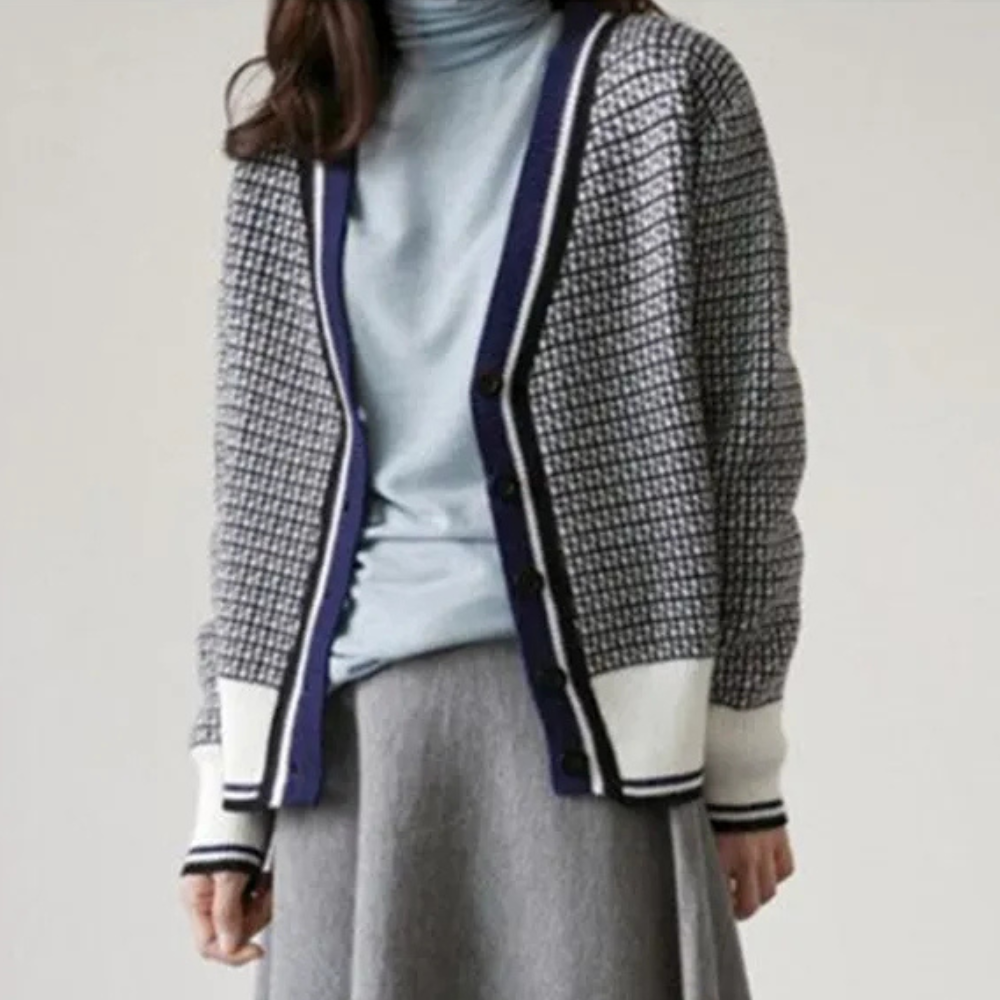 Grijze damescardigan met blauw-witte ruitpatroon, V-hals en knoopsluiting, gedragen over een lichtblauwe coltrui. Stijlvolle herfstmode.