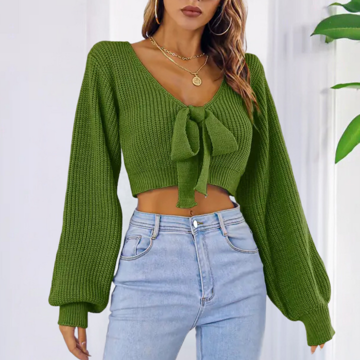 Vrouw draagt groene gebreide trui met strik, lange mouwen en V-hals, gecombineerd met lichtblauwe jeans. Modieuze dameskleding, herfststijl.