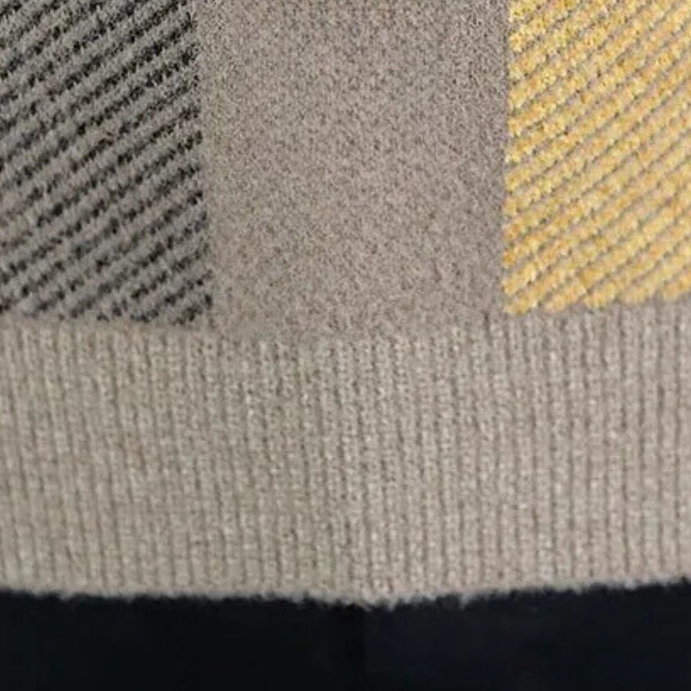 Grijze en gele gebreide trui met geribbelde textuur, close-up. Modieuze herenkleding, wintertrui, warme stoffen, stijlvolle patronen.