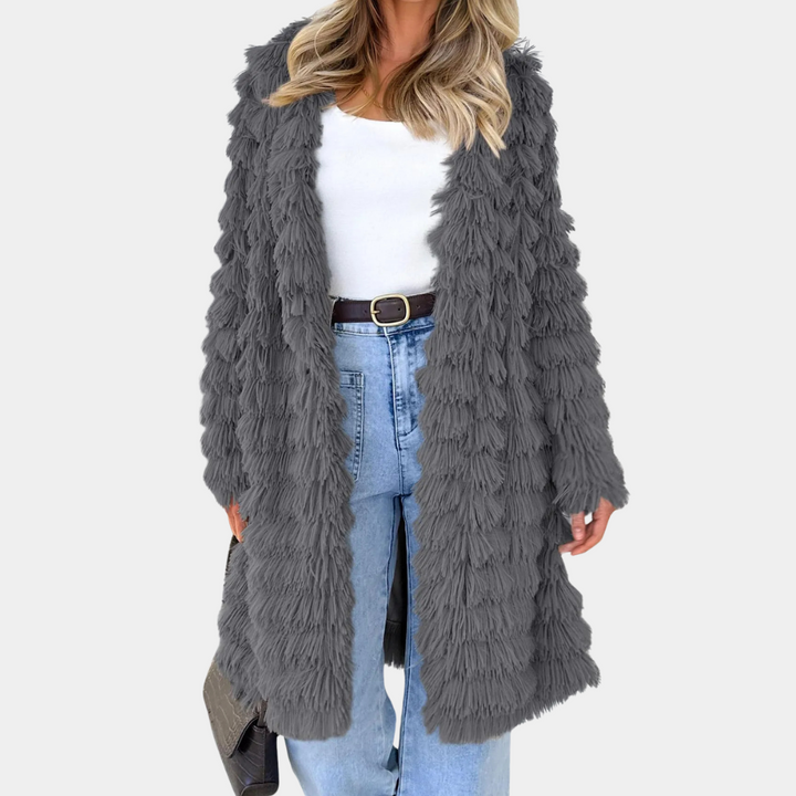 Grijze pluizige damesjas, open stijl, gecombineerd met witte top en blauwe jeans. Modieuze winterkleding, trendy en comfortabel.