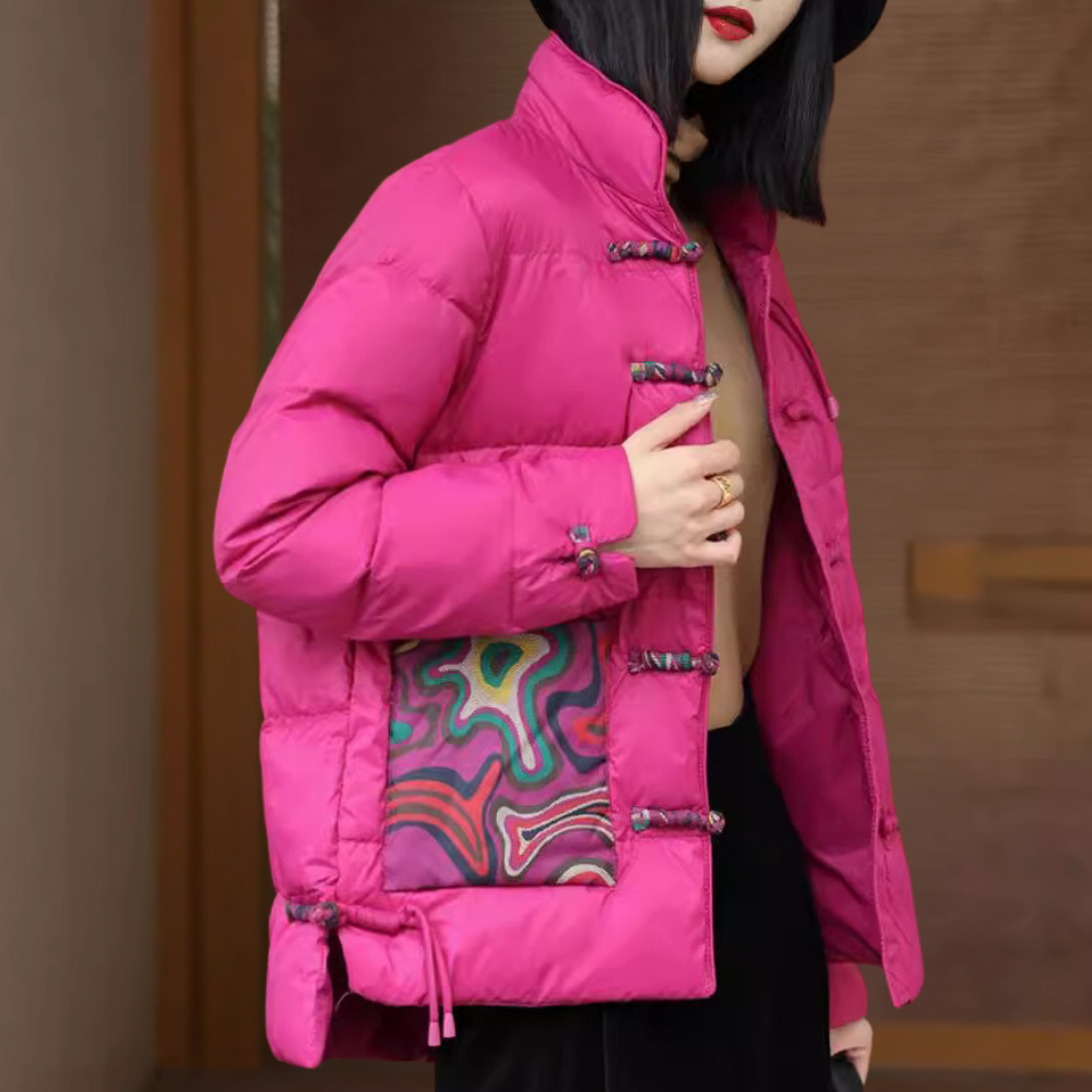 Vrouw in felroze gewatteerde jas met kleurrijk patroon, staande voor houten achtergrond. Modieuze winterjas, trendy dameskleding, warme bovenkleding.