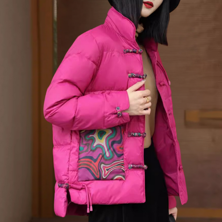 Vrouw in felroze gewatteerde jas met kleurrijk patroon, staande voor houten achtergrond. Modieuze winterjas, trendy dameskleding, warme bovenkleding.