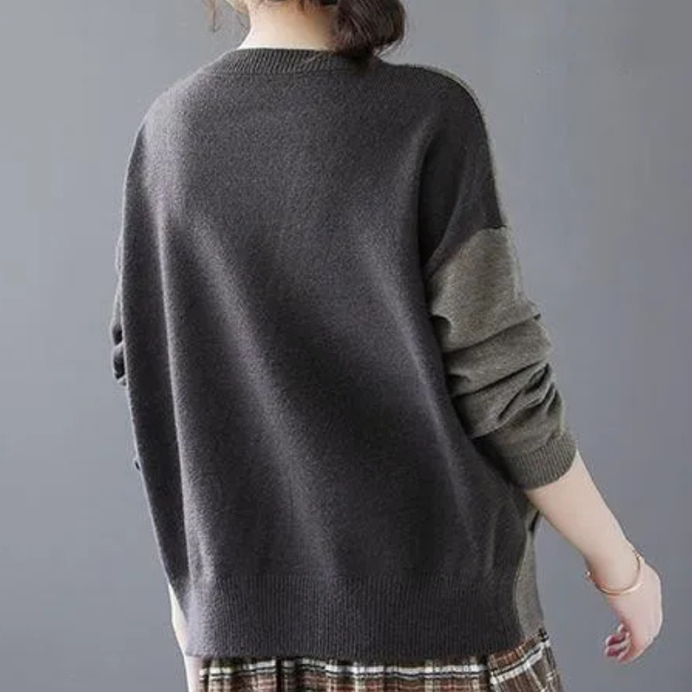 Vrouw draagt een oversized, donkergrijze trui met lange mouwen en een geruite rok. Modieuze herfstkleding, casual stijl, comfortabele outfit.