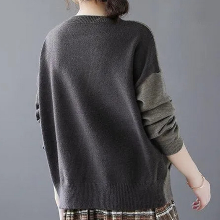 Vrouw draagt een oversized, donkergrijze trui met lange mouwen en een geruite rok. Modieuze herfstkleding, casual stijl, comfortabele outfit.