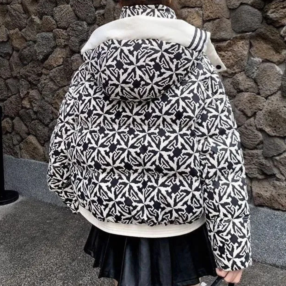 Zwart-witte gewatteerde jas met patroon, capuchon en rits, gedragen door persoon voor stenen muur. Modieuze winterjas, trendy streetwear.