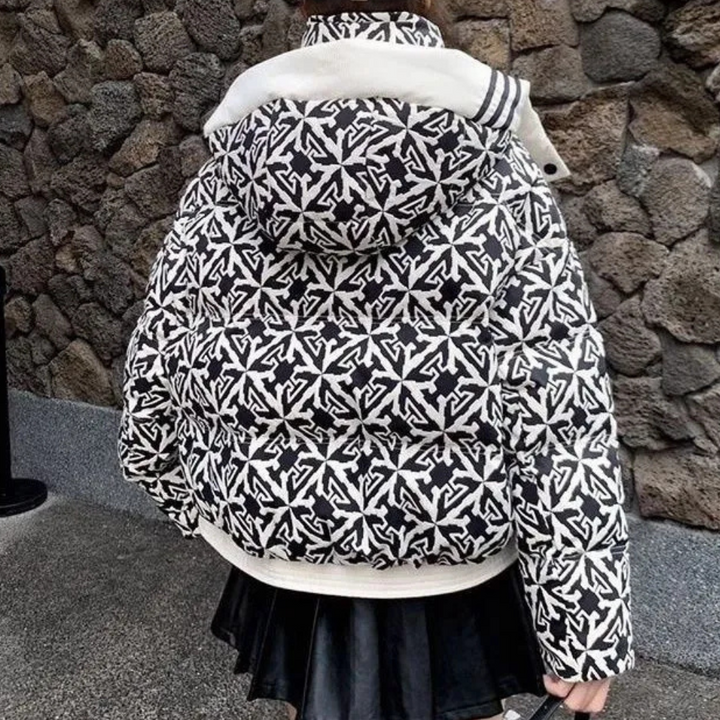 Zwart-witte gewatteerde jas met patroon, capuchon en rits, gedragen door persoon voor stenen muur. Modieuze winterjas, trendy streetwear.