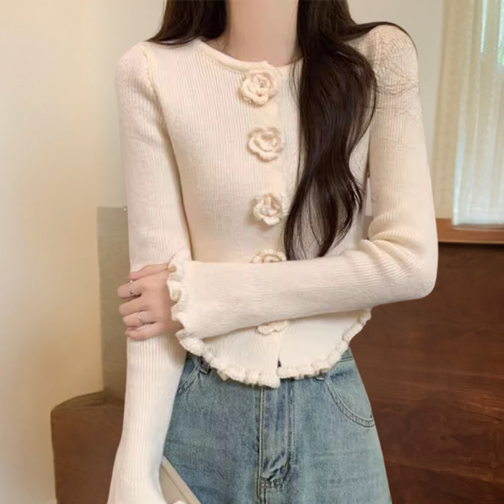 Witte gebreide damestrui met bloemenknopen, lange mouwen en geribbelde randen, gecombineerd met blauwe jeans. Modieuze casual outfit.