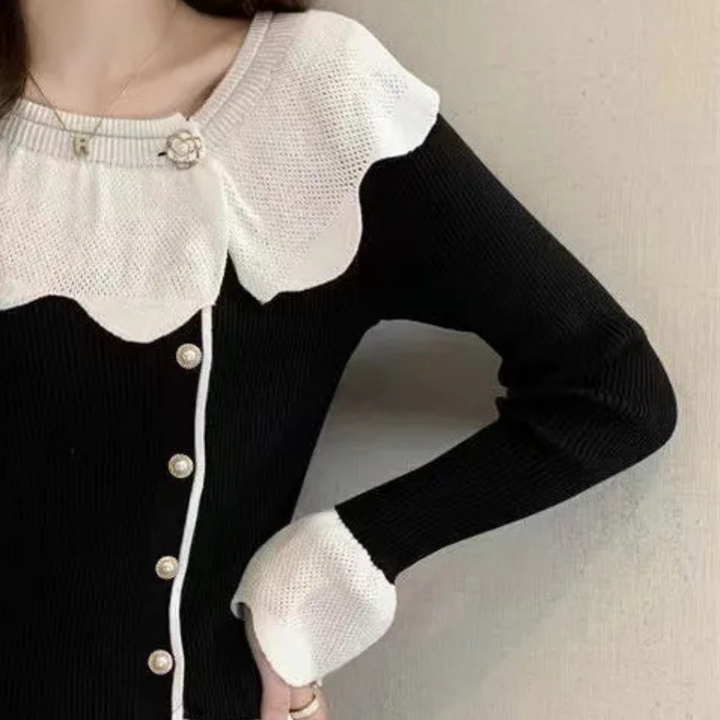 Vrouw draagt stijlvolle zwart-witte trui met parelknopen en bloemdetail, modieuze dameskleding, elegante herfstmode, trendy outfit.