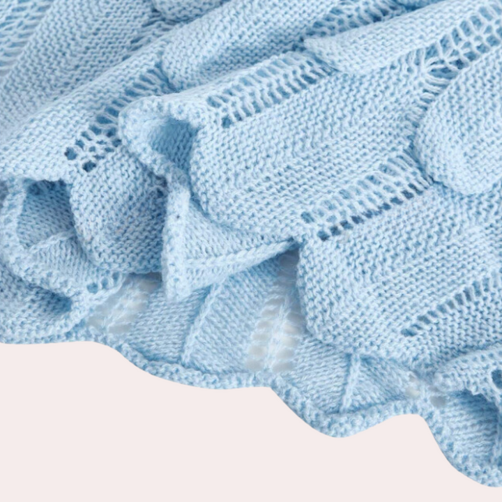 Lichtblauwe gebreide deken met golvende randen, gemaakt van zacht katoen. Perfect voor babykamers, kinderkamers en als decoratief woonaccessoire.