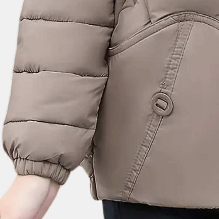 Beige gewatteerde winterjas met knoopdetail en zakken, close-up van mouw en hand. Modieuze damesjas, warme winterkleding, casual stijl.